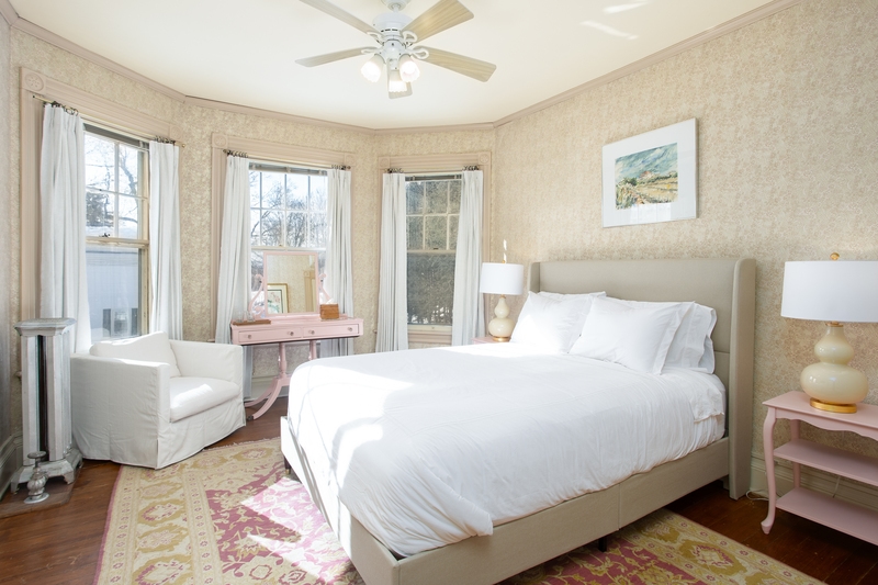 sunlit room with plush bed, pink vanity, armchair, cozy pink rug