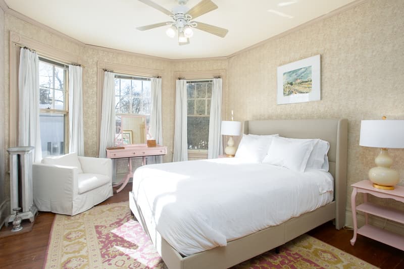 sunlit room with plush bed, pink vanity, armchair, cozy pink rug