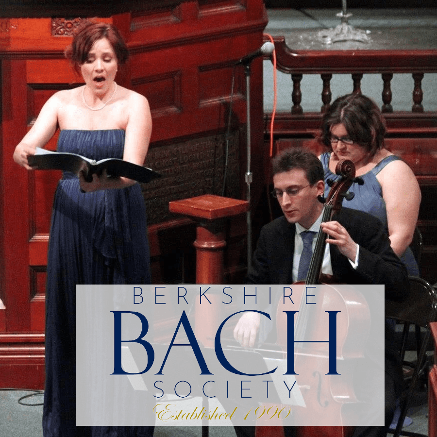 A soprano performs on stage while a cellist accompanies her, with a woman seated behind them.