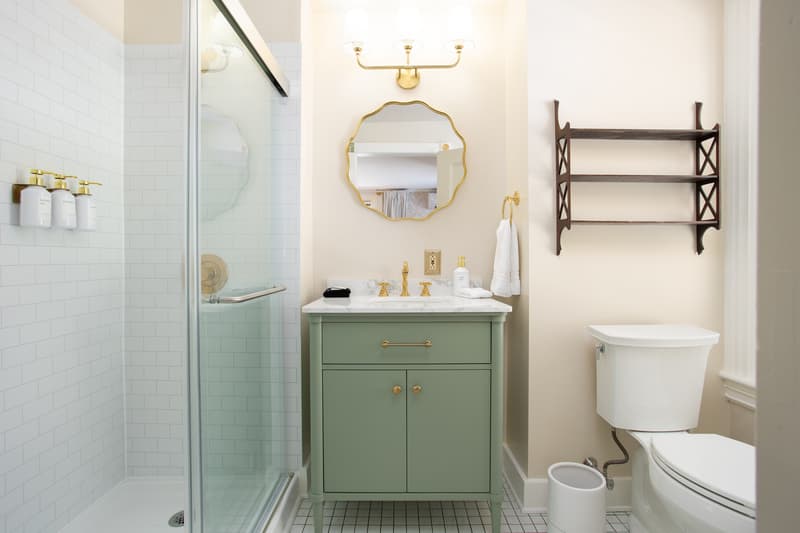 A modern bathroom featuring a glass shower, green vanity, gold fixtures, and a wall shelf.