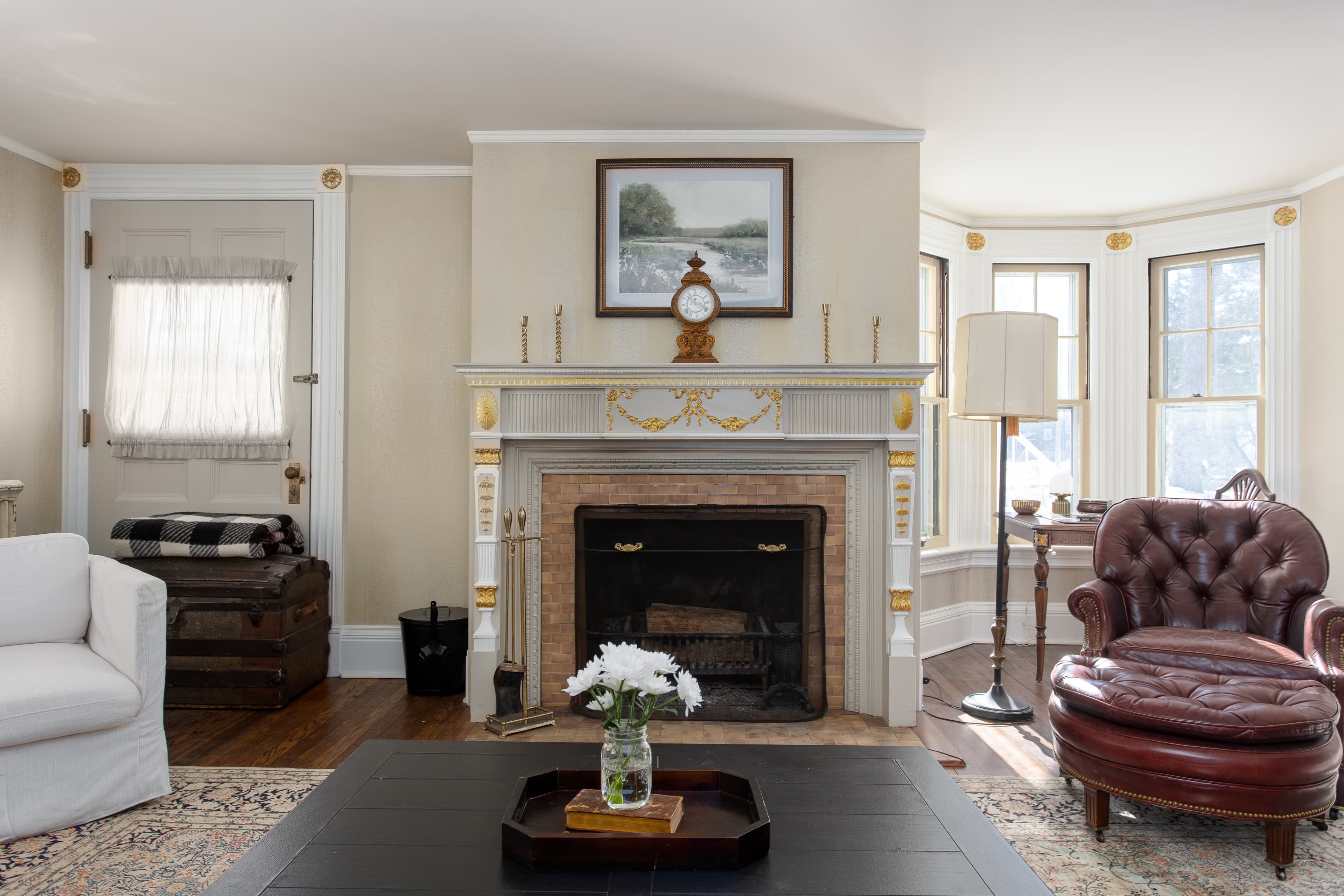 Cozy living room featuring a vintage fireplace, a comfortable armchair, and large windows.