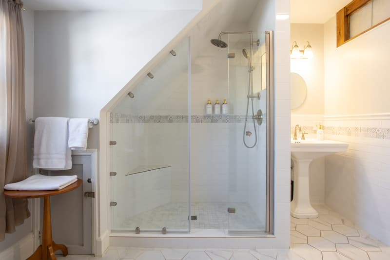 A modern bathroom featuring a glass shower, a pedestal sink, and a wooden stool.