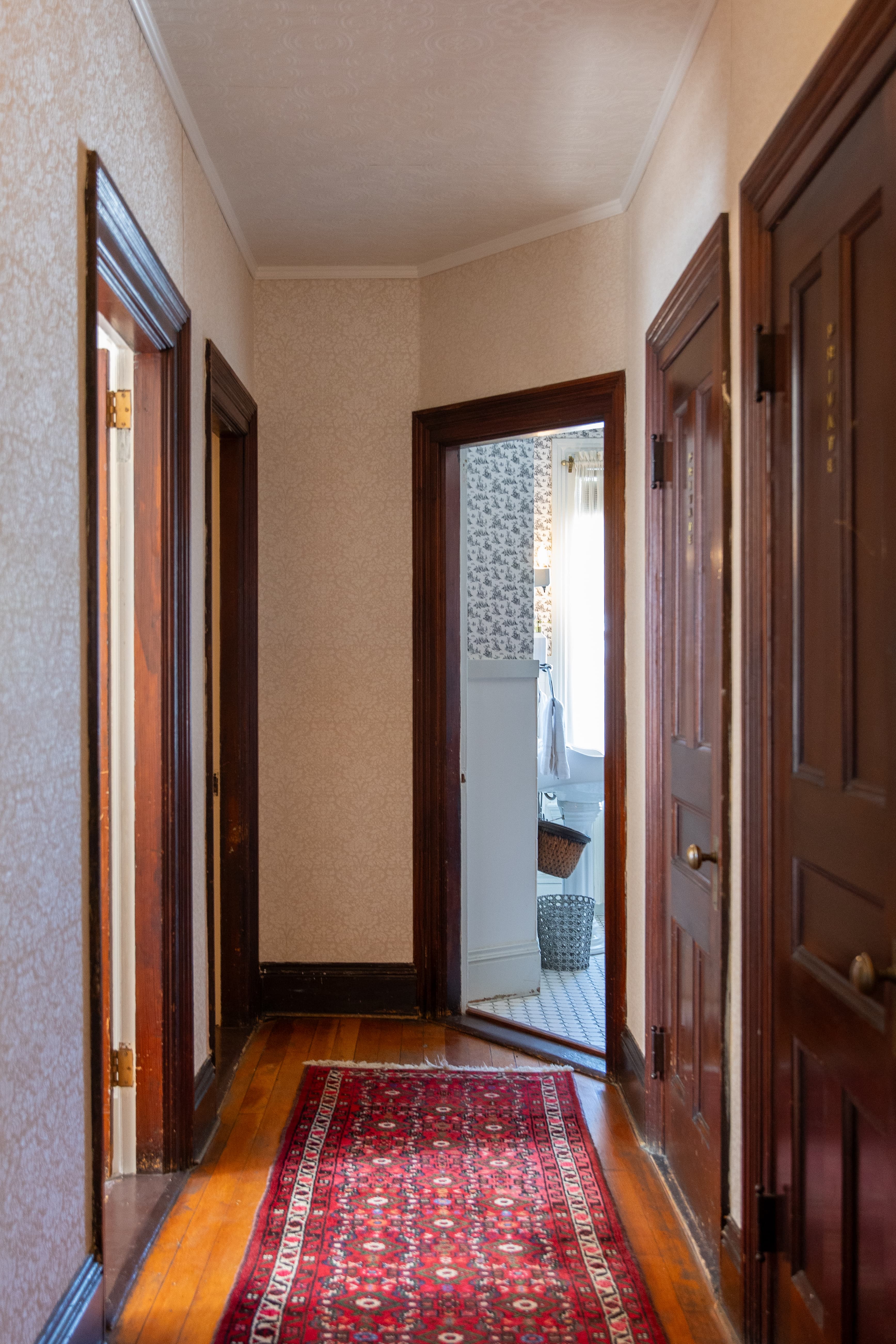 A hallway featuring wooden doors and a patterned rug, leading to a bathroom.