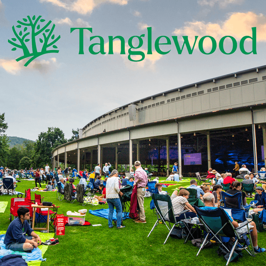 A large audience gathers on green grass at Tanglewood for an outdoor event, with a curved building in the background.