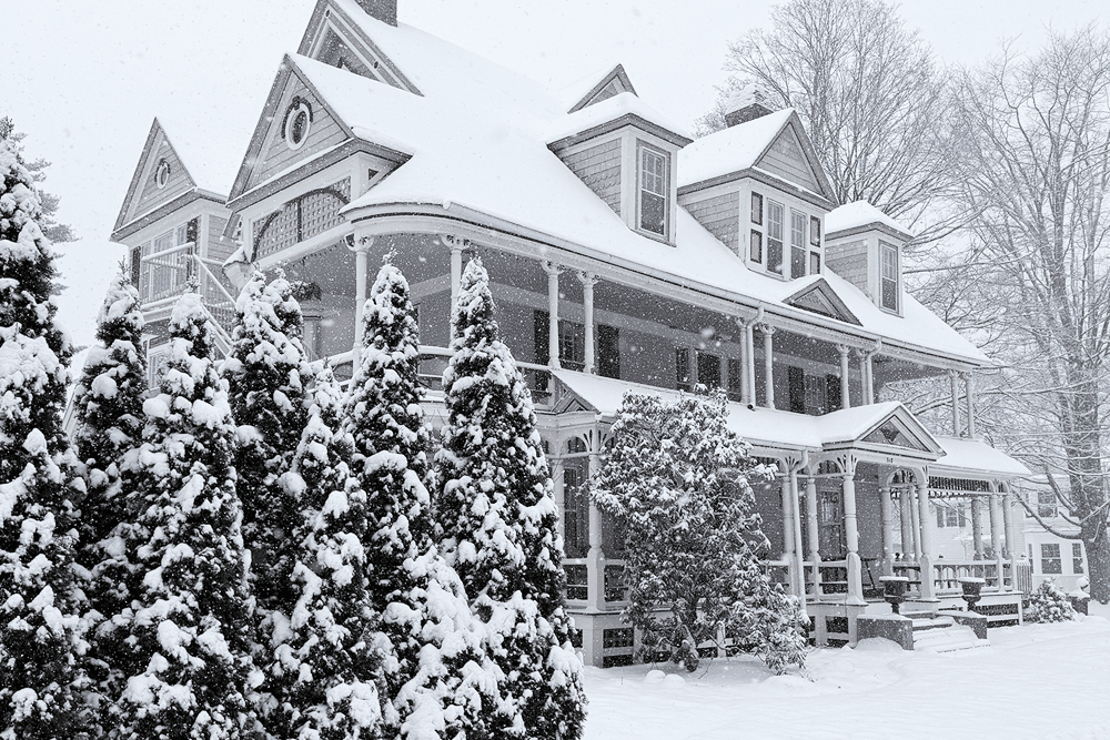 A large, Victorian-style house surrounded by snow-covered trees on a snowy winter day.
