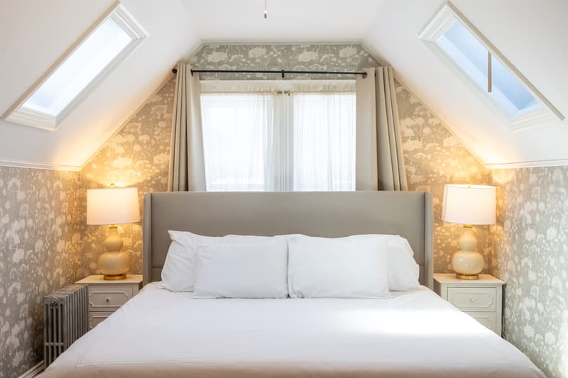 A cozy attic bedroom featuring a gray upholstered bed, soft lighting, and patterned wallpaper.