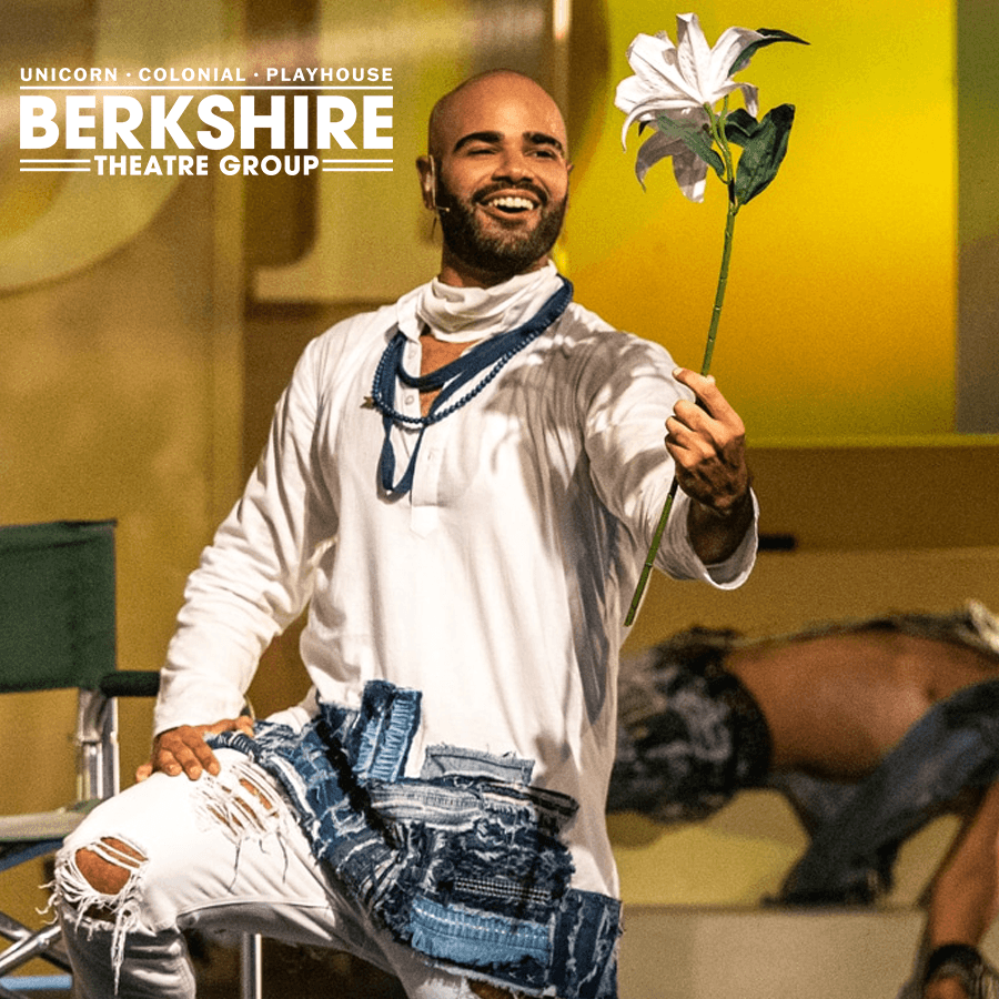 A performer in a white outfit holds a lily while smiling on stage.