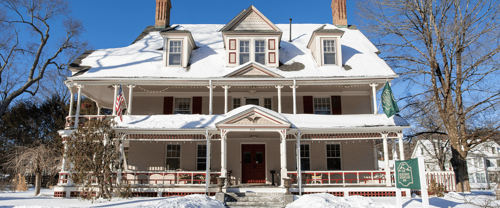 A large historic house covered in snow with a red door and flags in front.