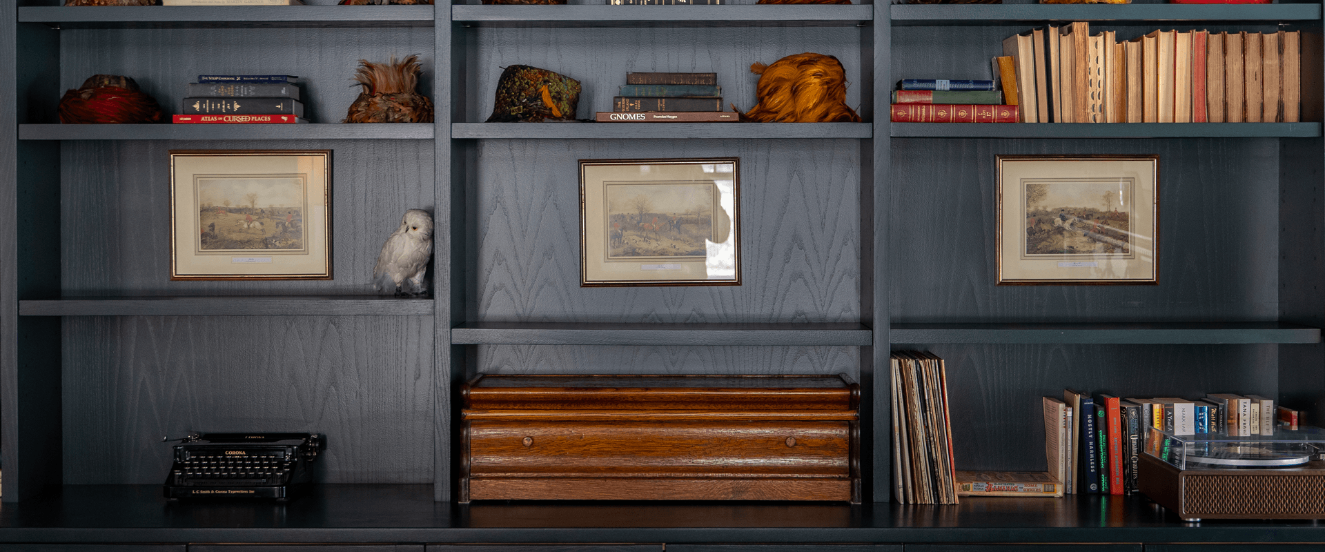 A dark wooden bookshelf filled with books, framed pictures, and decorative items, including a typewriter and a figurine of an owl.
