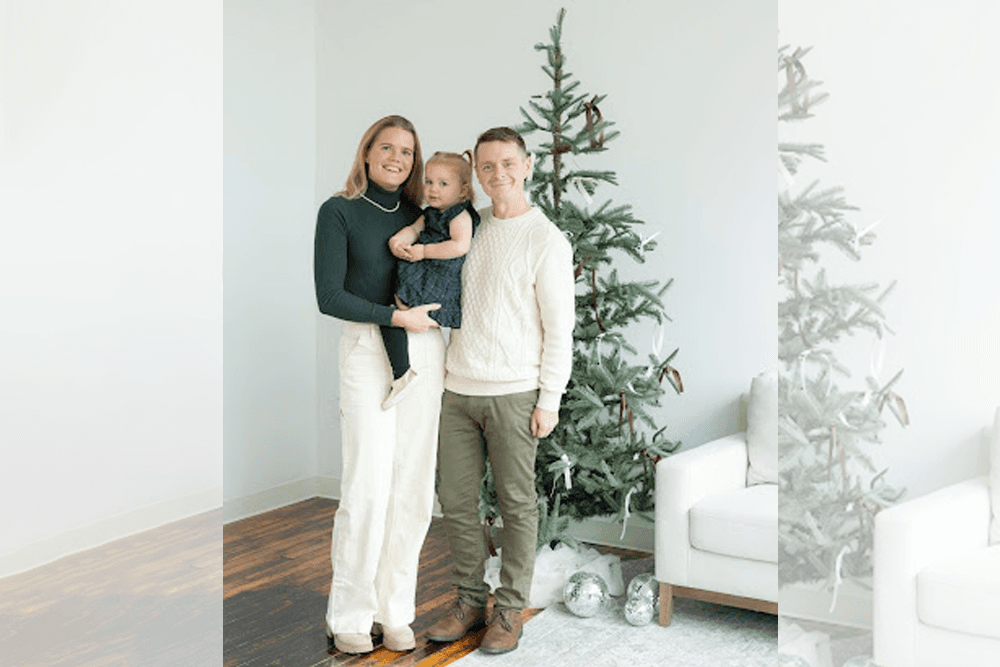 A family poses together in front of a Christmas tree, with one parent holding a young child.